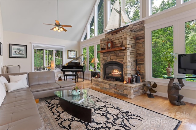 living area with baseboards, ceiling fan, wood finished floors, a stone fireplace, and high vaulted ceiling