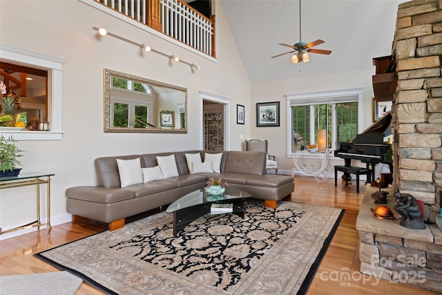 living room featuring ceiling fan, a high ceiling, light wood-style flooring, and baseboards