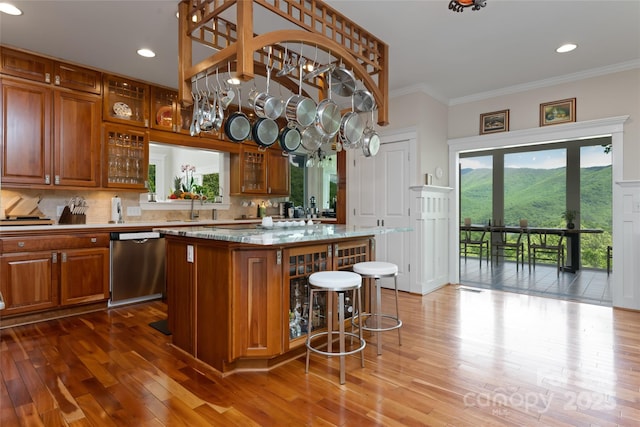 kitchen featuring brown cabinets, stainless steel dishwasher, glass insert cabinets, a kitchen island, and light stone countertops