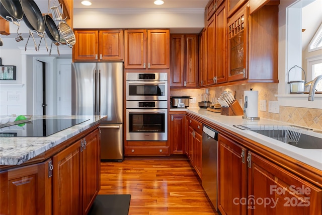 kitchen featuring stainless steel appliances, backsplash, brown cabinetry, ornamental molding, and a sink