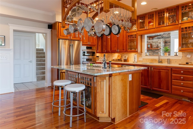 kitchen with an island with sink, glass insert cabinets, light stone counters, ornamental molding, and a sink