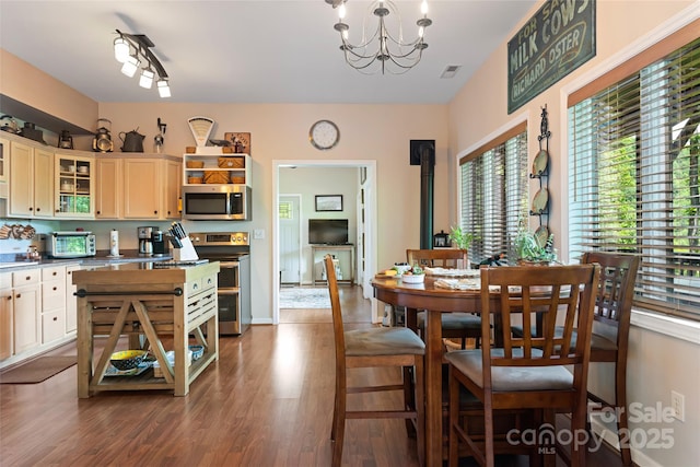 dining space featuring a toaster, wood finished floors, visible vents, a wood stove, and an inviting chandelier