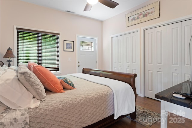 bedroom with multiple closets, visible vents, dark wood-type flooring, and a ceiling fan