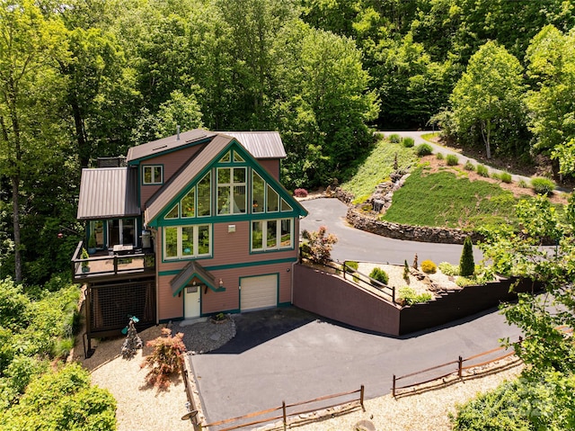 rustic home with driveway, a view of trees, metal roof, an attached garage, and a wooden deck