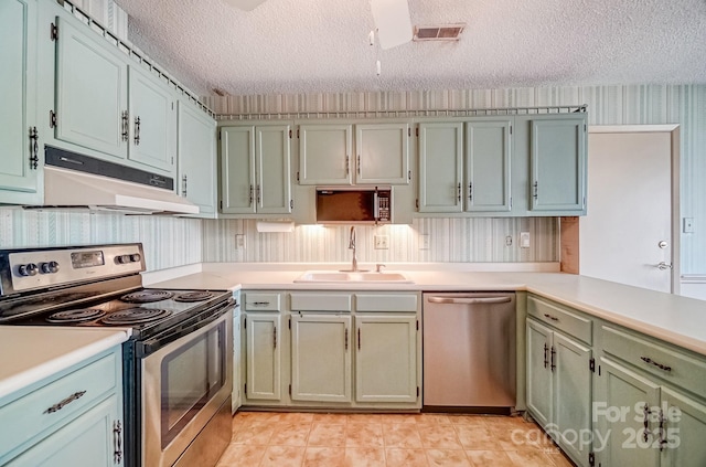 kitchen featuring visible vents, a sink, under cabinet range hood, appliances with stainless steel finishes, and wallpapered walls