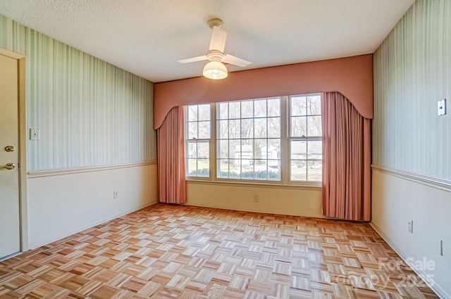 spare room with a textured ceiling, ceiling fan, and wallpapered walls