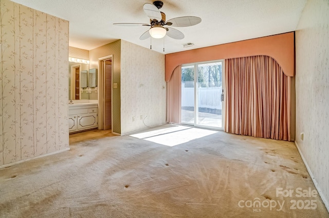 empty room featuring visible vents, wallpapered walls, carpet, a textured ceiling, and a ceiling fan