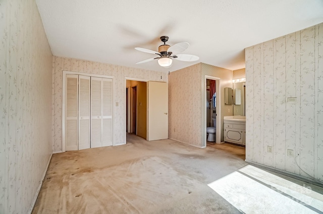 unfurnished bedroom with ensuite bathroom, a ceiling fan, a closet, carpet floors, and wallpapered walls