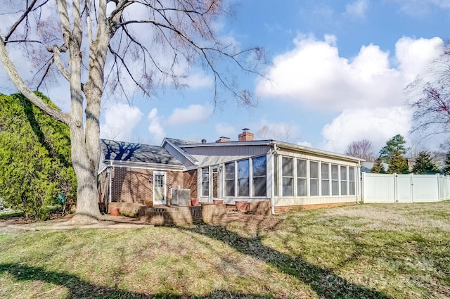 back of property with fence, a yard, a sunroom, brick siding, and a chimney