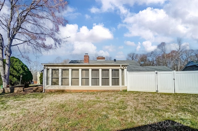 rear view of house featuring a gate, fence, a sunroom, a chimney, and a lawn