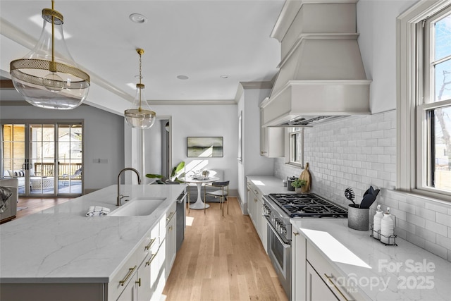 kitchen featuring custom exhaust hood, hanging light fixtures, stainless steel appliances, light stone counters, and sink