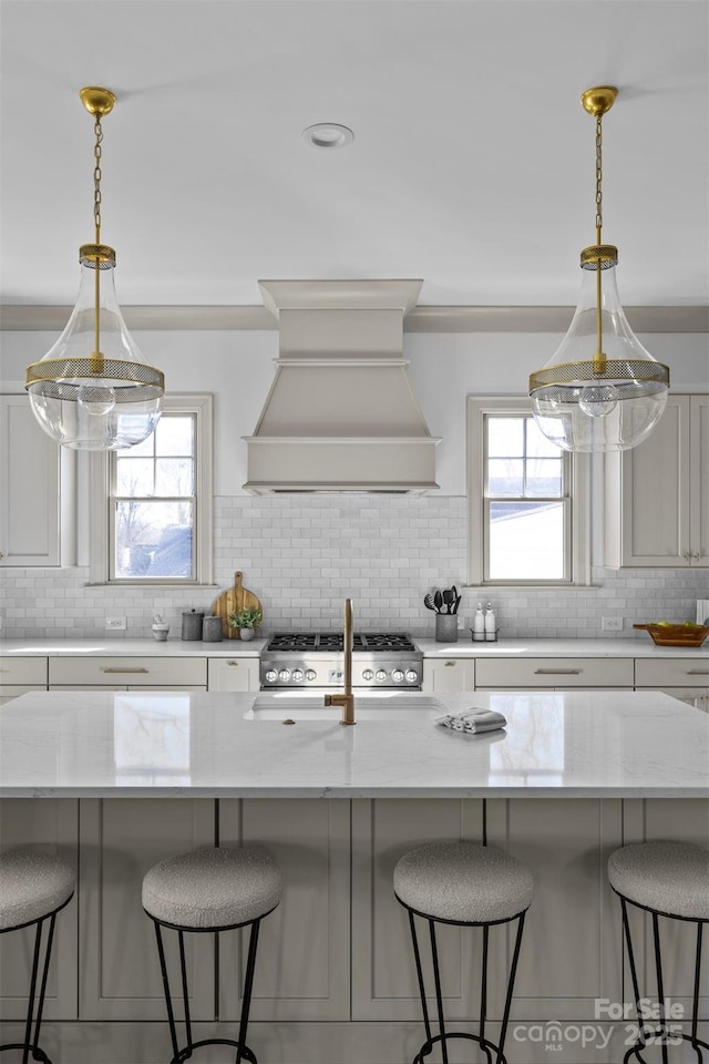 kitchen featuring a kitchen breakfast bar, custom exhaust hood, stove, and hanging light fixtures