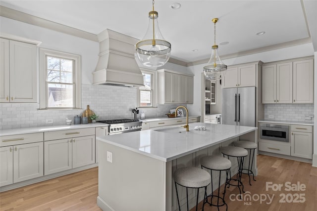 kitchen with sink, custom range hood, stove, high end refrigerator, and a center island with sink