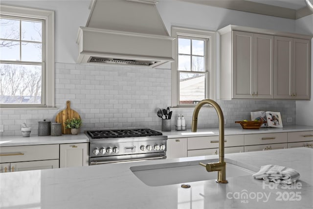 kitchen featuring backsplash, premium range hood, white cabinets, gas stove, and light stone countertops