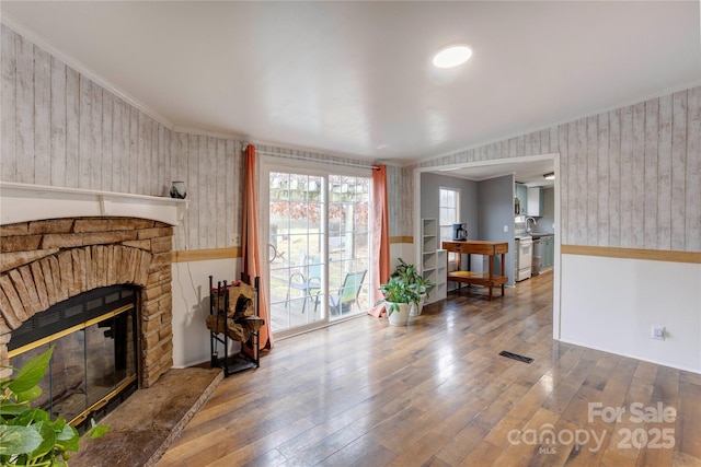 living room with crown molding, hardwood / wood-style floors, a stone fireplace, and sink