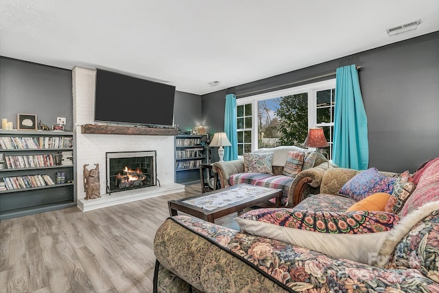 living room featuring a brick fireplace, wood finished floors, and visible vents