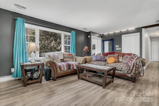 living area with light wood-type flooring, visible vents, and baseboards