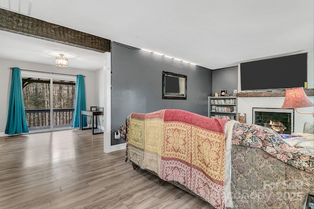 bedroom with wood finished floors, baseboards, visible vents, a warm lit fireplace, and access to exterior