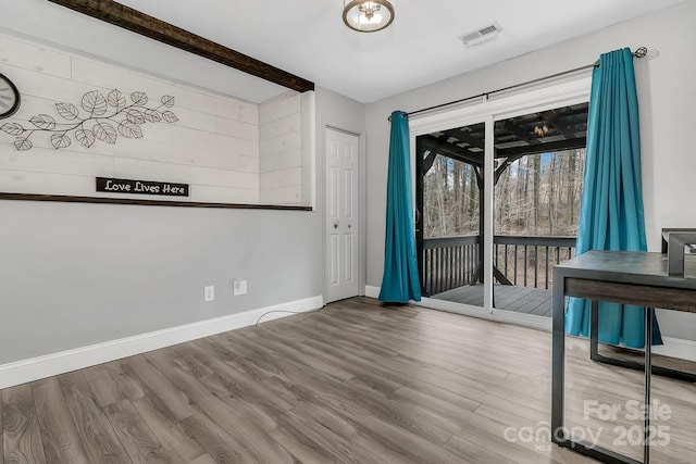 empty room with beam ceiling, visible vents, baseboards, and wood finished floors