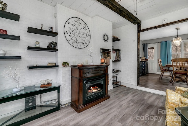 living area with beam ceiling, wood finished floors, brick wall, and a lit fireplace