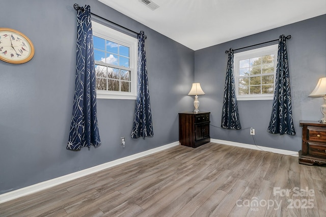 spare room with wood finished floors, visible vents, and baseboards