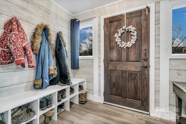 mudroom with light wood-style floors, wood walls, and ornamental molding