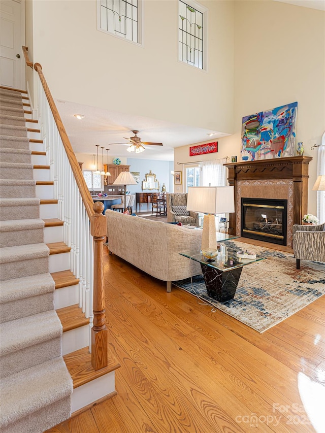 living room featuring a fireplace, light hardwood / wood-style flooring, ceiling fan, and a high ceiling