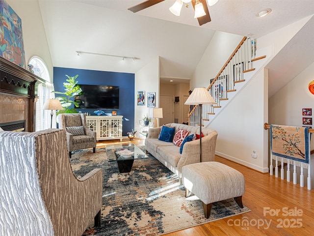 living room featuring lofted ceiling, rail lighting, light wood-type flooring, a tile fireplace, and ceiling fan