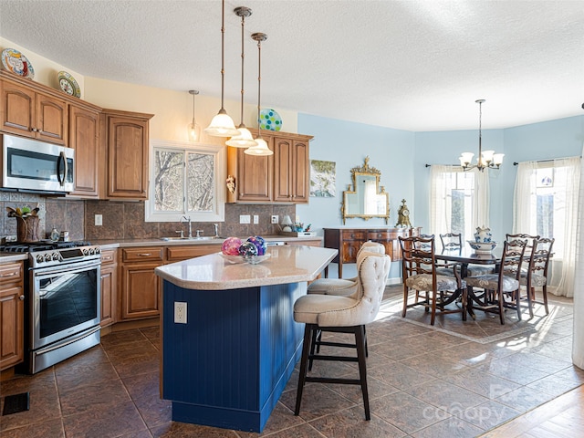 kitchen with a kitchen island, appliances with stainless steel finishes, decorative light fixtures, sink, and backsplash