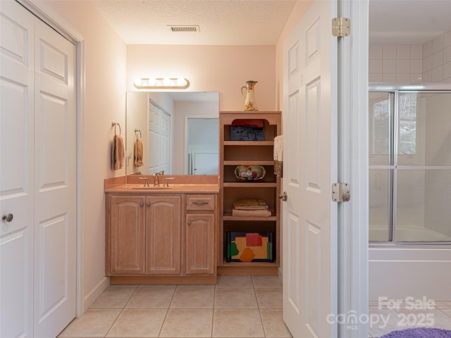 bathroom featuring vanity, bath / shower combo with glass door, tile patterned floors, and a textured ceiling