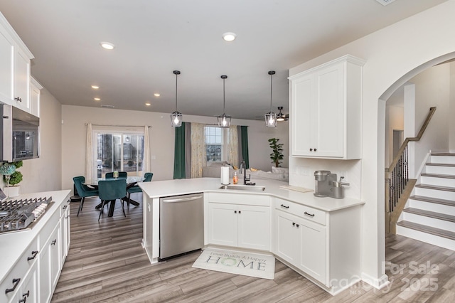 kitchen featuring appliances with stainless steel finishes, hanging light fixtures, light countertops, white cabinetry, and a sink