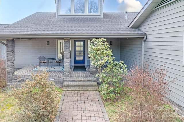 property entrance with covered porch, a shingled roof, and brick siding