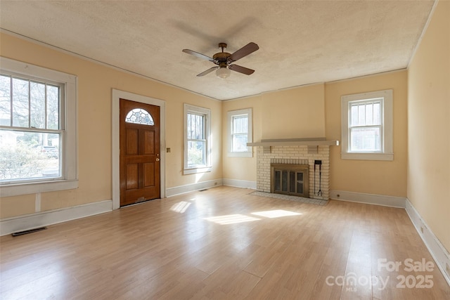 entryway with a brick fireplace, a healthy amount of sunlight, a textured ceiling, and light wood-type flooring