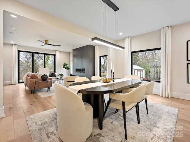 dining area featuring a large fireplace, baseboards, ceiling fan, recessed lighting, and light wood-style floors