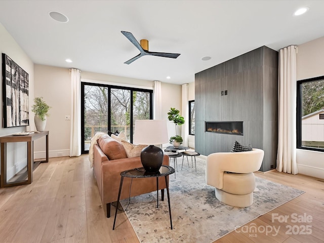 living room with recessed lighting, a ceiling fan, light wood-type flooring, and a large fireplace