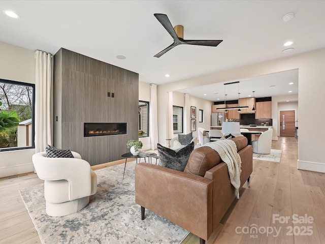 living room with baseboards, recessed lighting, a fireplace, light wood-style floors, and a ceiling fan