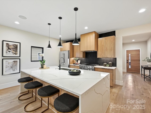 kitchen featuring light wood-style flooring, backsplash, a kitchen island with sink, and appliances with stainless steel finishes