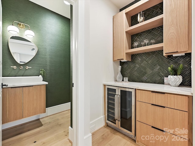 bar with light wood-style flooring, baseboards, backsplash, and beverage cooler