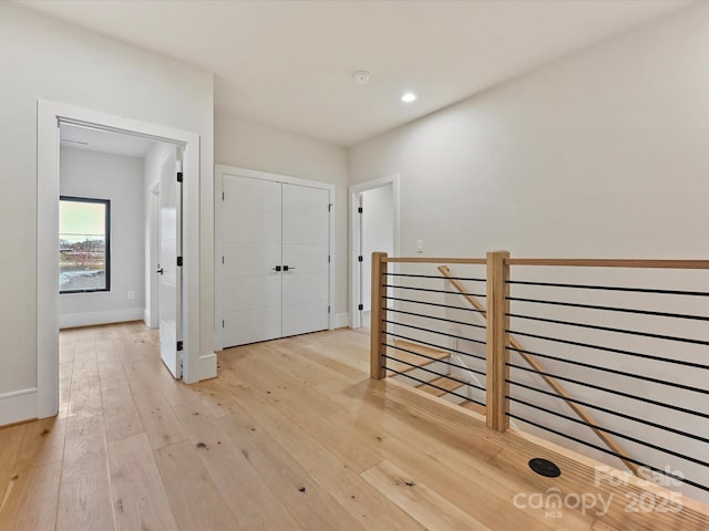 corridor featuring light wood finished floors, an upstairs landing, recessed lighting, and baseboards