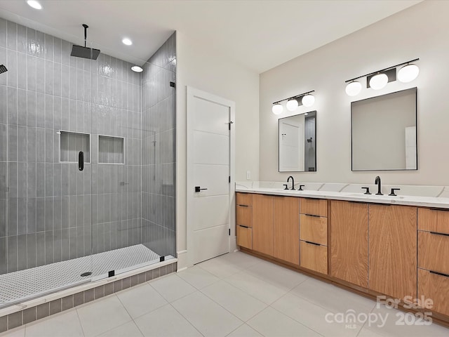 bathroom featuring tile patterned flooring, double vanity, a tile shower, and a sink