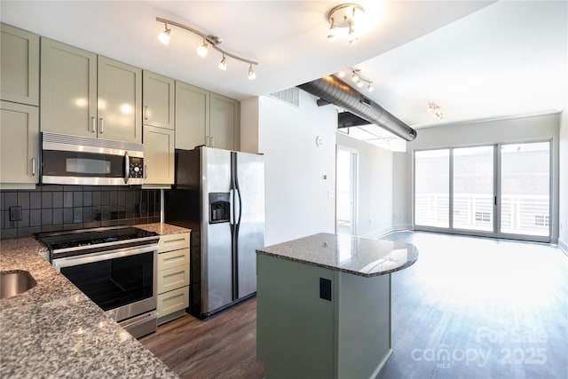 kitchen featuring a kitchen island, dark stone counters, stainless steel appliances, dark wood-type flooring, and tasteful backsplash