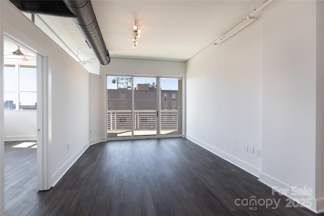 spare room featuring rail lighting, baseboards, and dark wood-style flooring