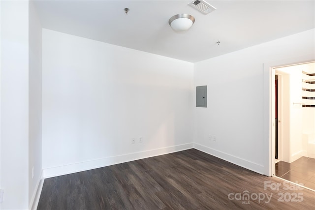 empty room with electric panel, visible vents, baseboards, and dark wood-style floors