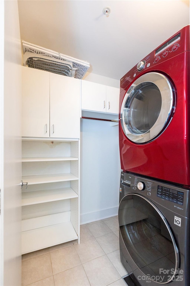 washroom with light tile patterned floors, cabinet space, stacked washer and clothes dryer, and baseboards