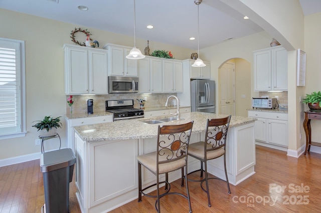 kitchen featuring an island with sink, decorative light fixtures, sink, appliances with stainless steel finishes, and white cabinets