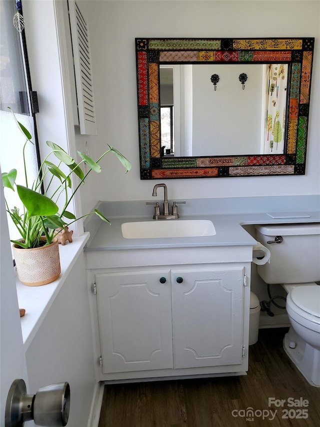 half bathroom with vanity, toilet, and wood finished floors