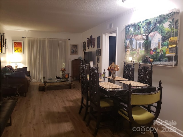 dining area featuring ornamental molding, visible vents, a textured ceiling, and wood finished floors