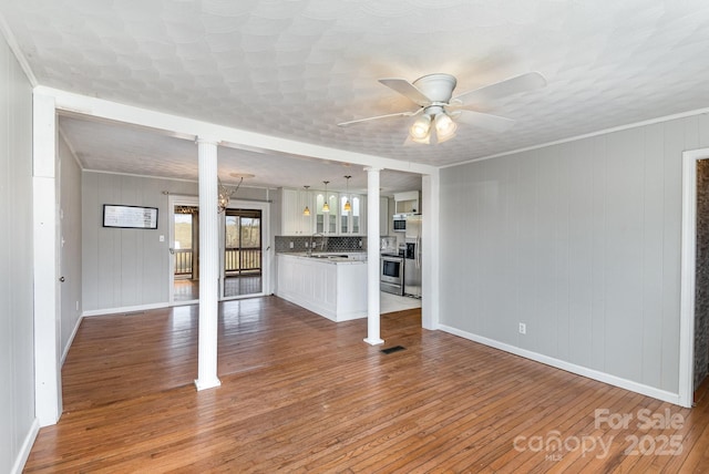 unfurnished living room with ceiling fan, baseboards, wood finished floors, decorative columns, and a sink