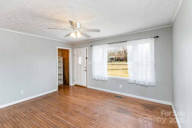 spare room featuring baseboards, wood finished floors, visible vents, crown molding, and a ceiling fan