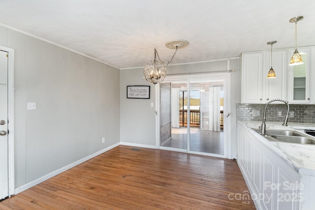 unfurnished dining area featuring baseboards, a chandelier, crown molding, a sink, and wood finished floors